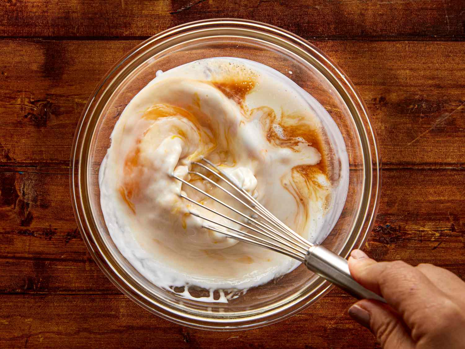 Hand whisking milk and liquid ingredients in a glass bowl