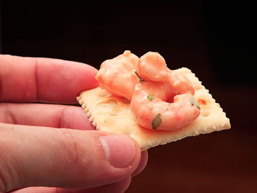 Hand holding a saltine cracker topped with Colombian shrimp cocktail.
