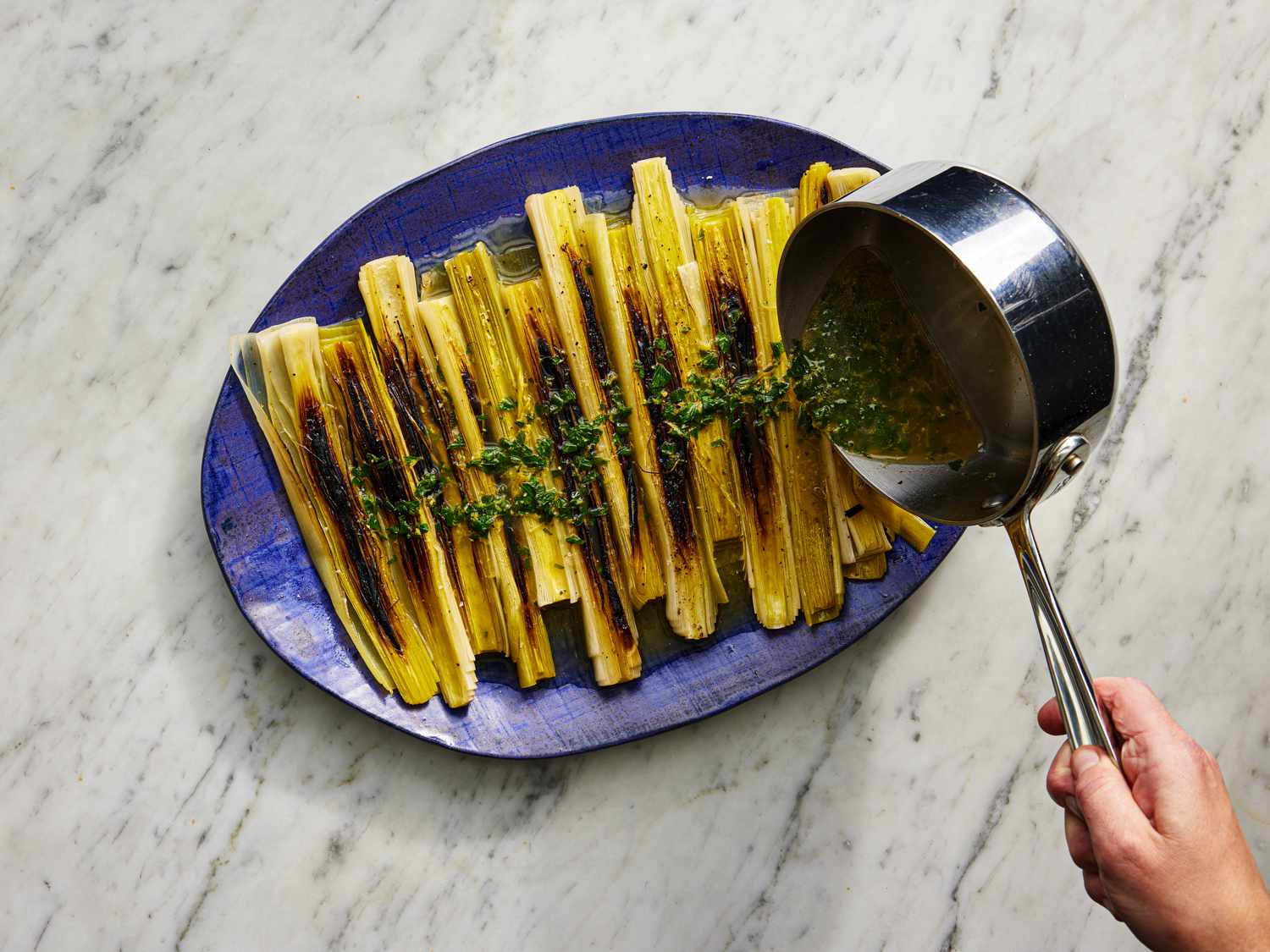 Overhead view of braising sauce being poured over plated finished leeks 