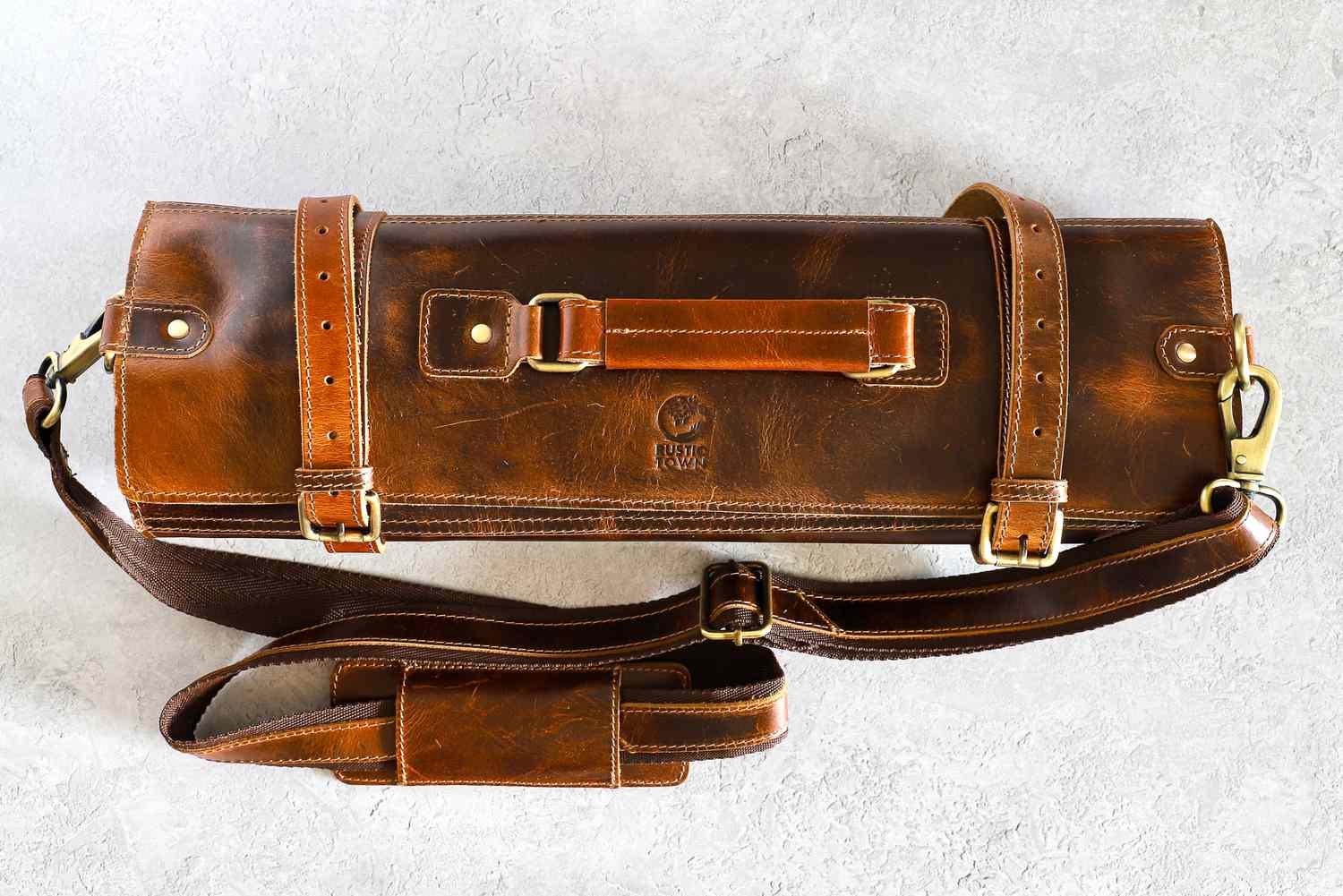 Rustic Town Genuine Leather Chef Knife Roll with straps and a handle placed on a gray surface