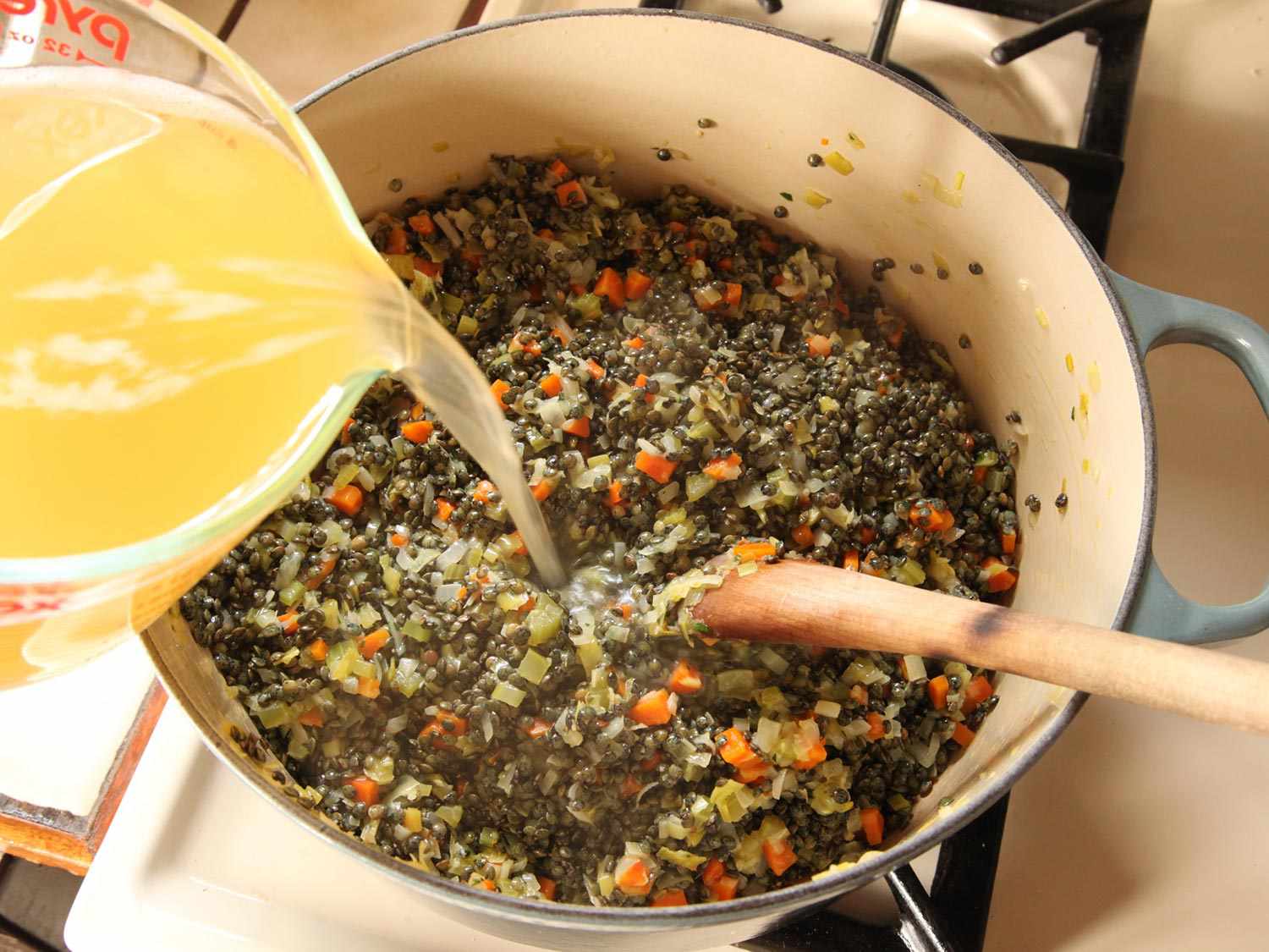 Adding stock to lentil soup.
