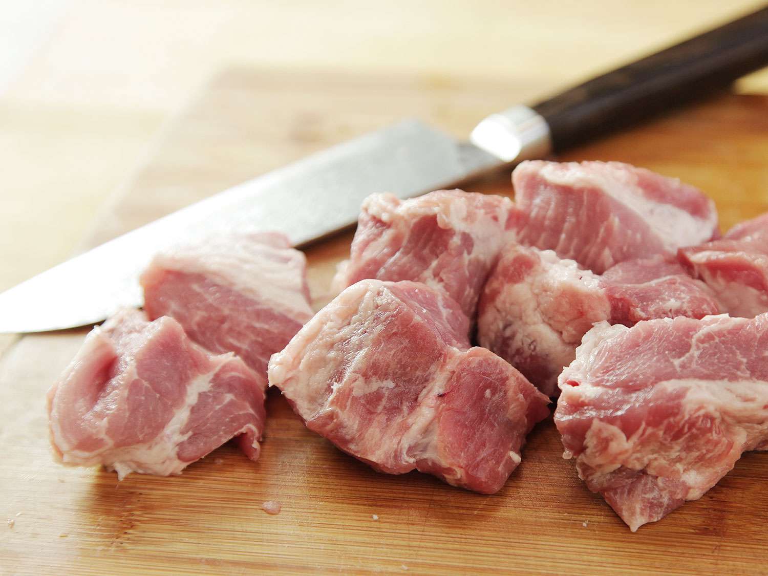 A knife and raw chunks of pork shoulder for chile verde stew.