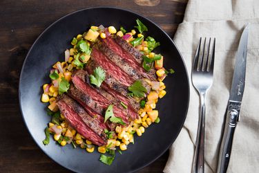 Overhead view of Skirt Steak With Warm Spicy Corn-and-Peach Salsa, served on a black plate.