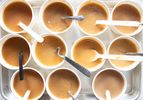 A tray of cups filled with gravy samples each containing a spoon or utensil for tasting