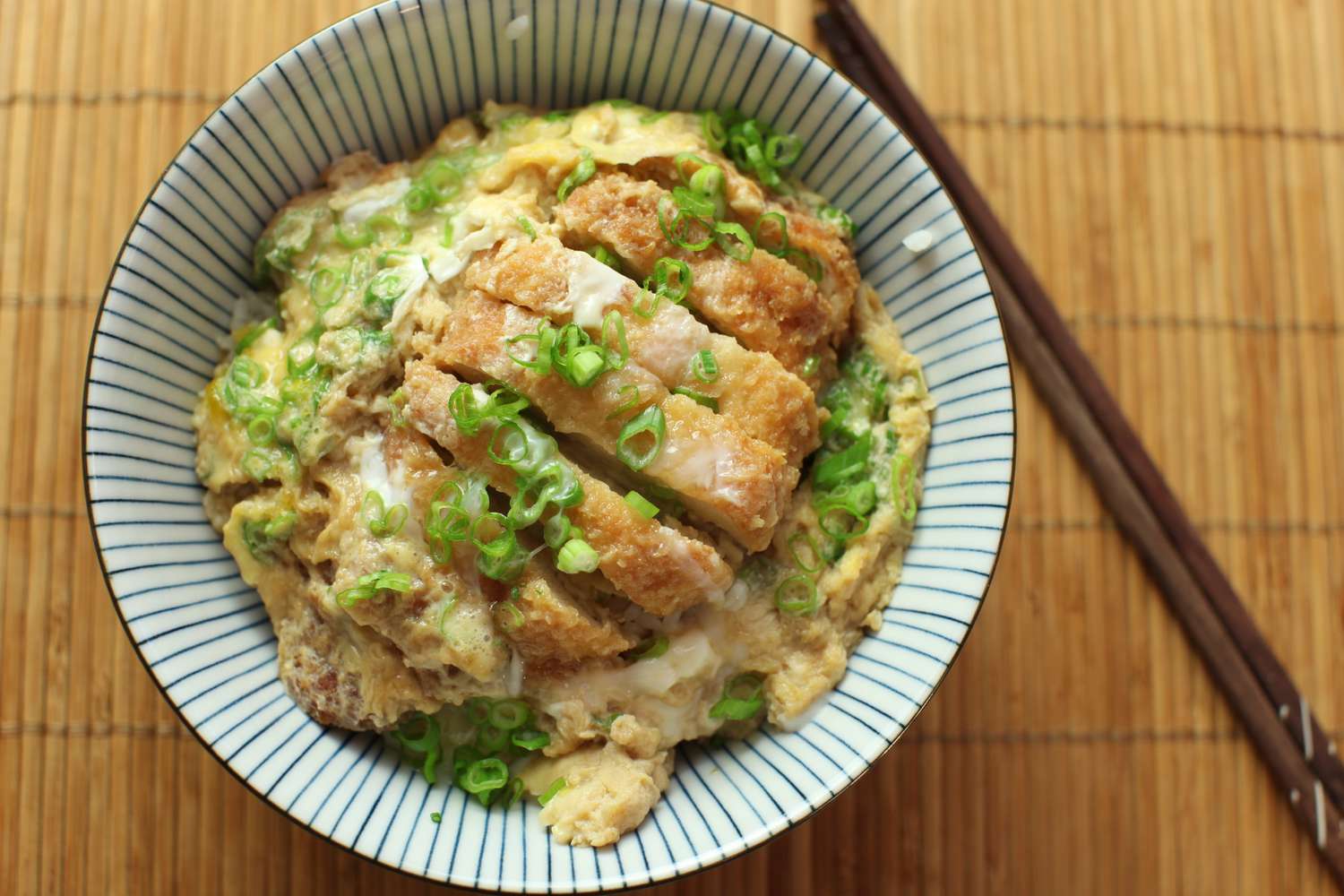 Overhead view of a bowl of katsudon, sprinkled with chopped green onion.