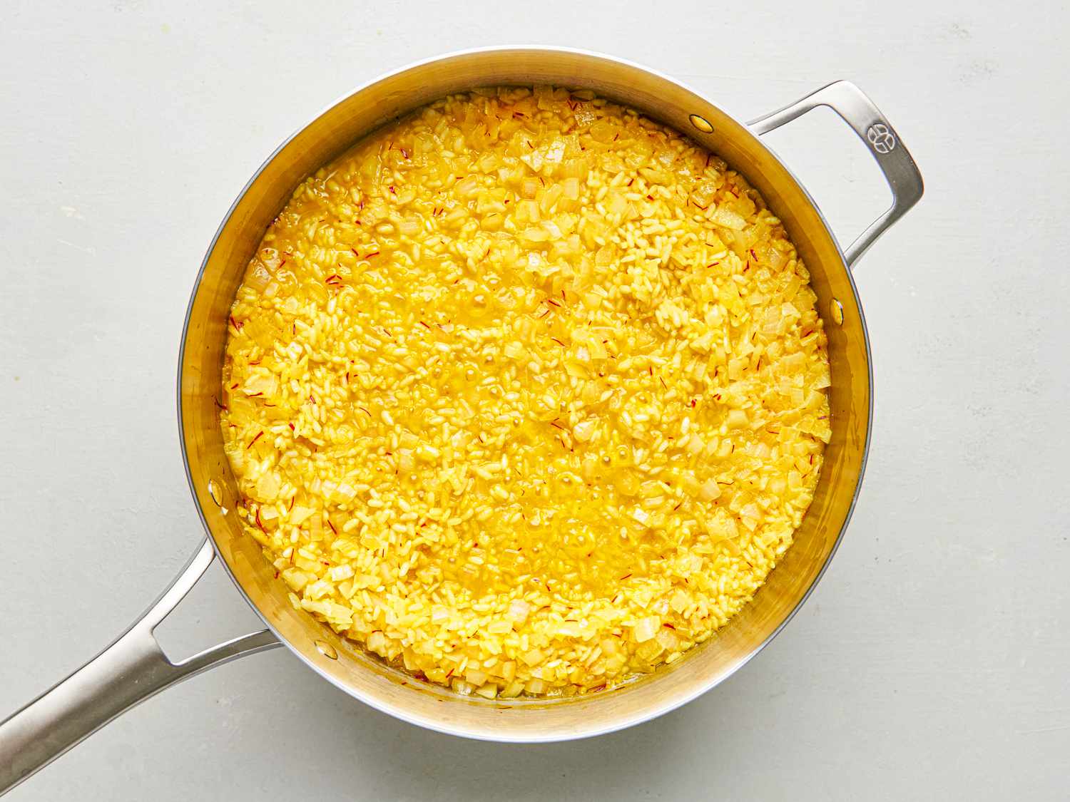 Saffron and stock added to the pan of rice. The rice is golden yellow from the saffron.