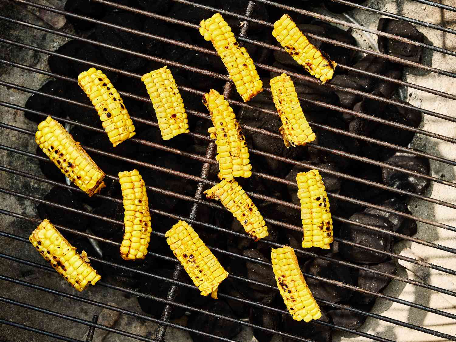 thin pieces of corn cooking over a grill with charcoal 