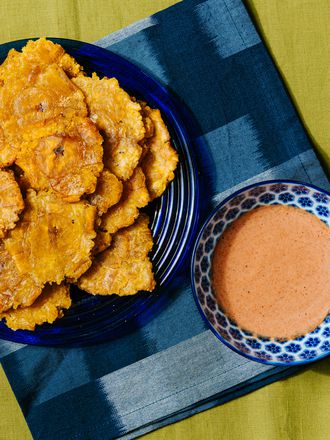 Overhead view of tostones on a blue plate with a blue napkin and bowl of dipping sauce