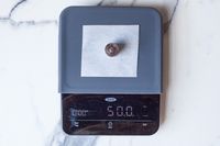 A chocolate chip on parchment paper placed on a kitchen scale reading 50 g