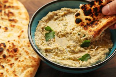 Dipping pita bread into baba ganoush in a small bowl, drizzled with olive oil.