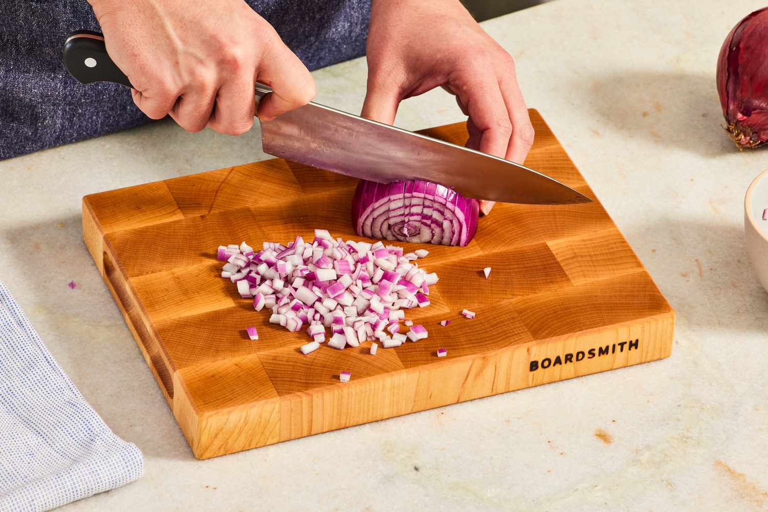 A person chopping a red onion a The Boardsmith wooden cutting board.