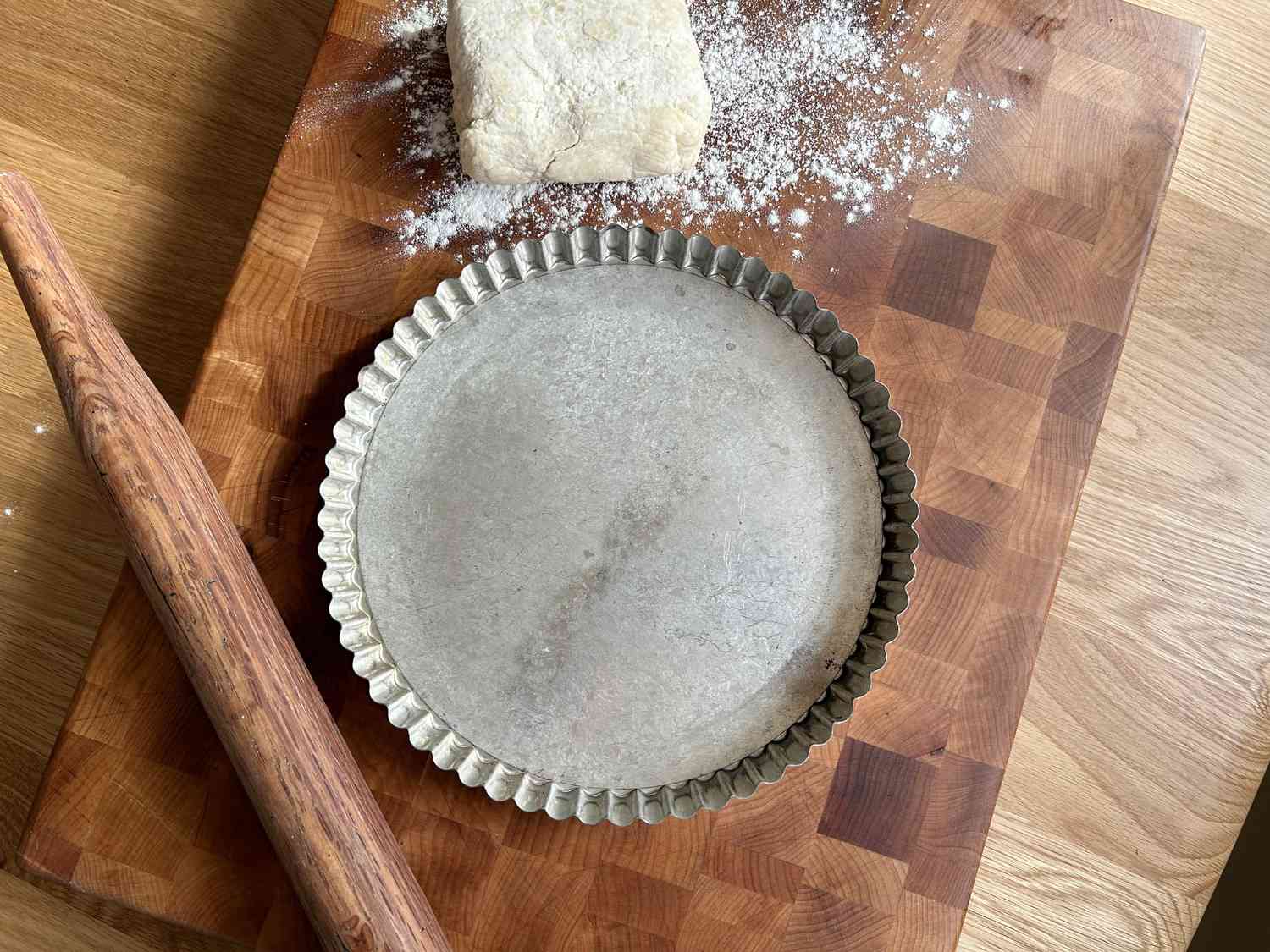 A metal tart pan on a wooden cutting board with dough and a rolling pin