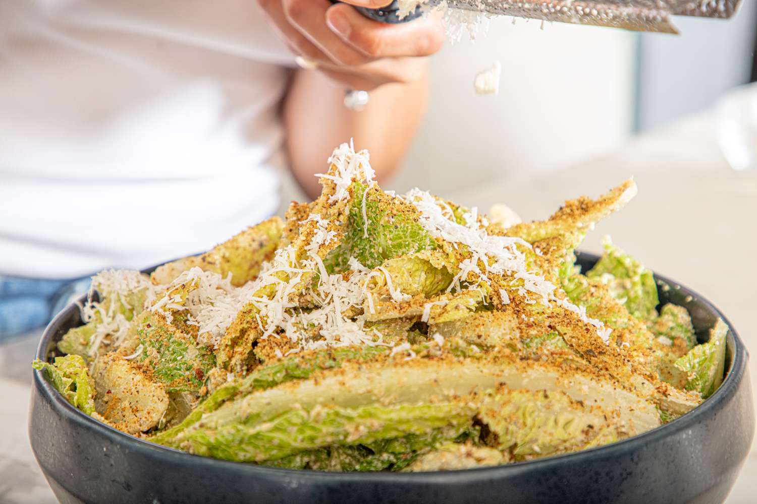 Caesar salad with grated cheese and seasoning being prepared in a bowl