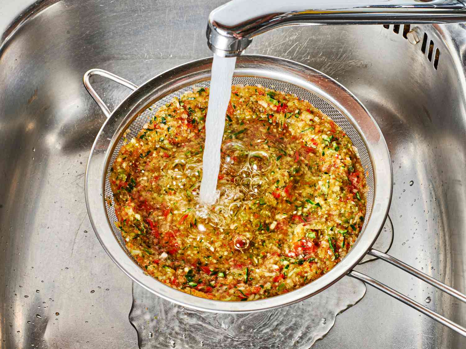 Rinsing vegetable mixture in fine mesh strainer under cold water