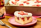A piece of strawberry poke cake on a plate tray with more in the background