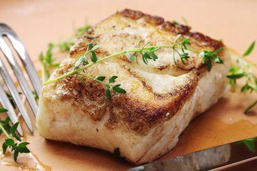 Butter-based sous vide and seared halibut with a sprig of thyme on top. 