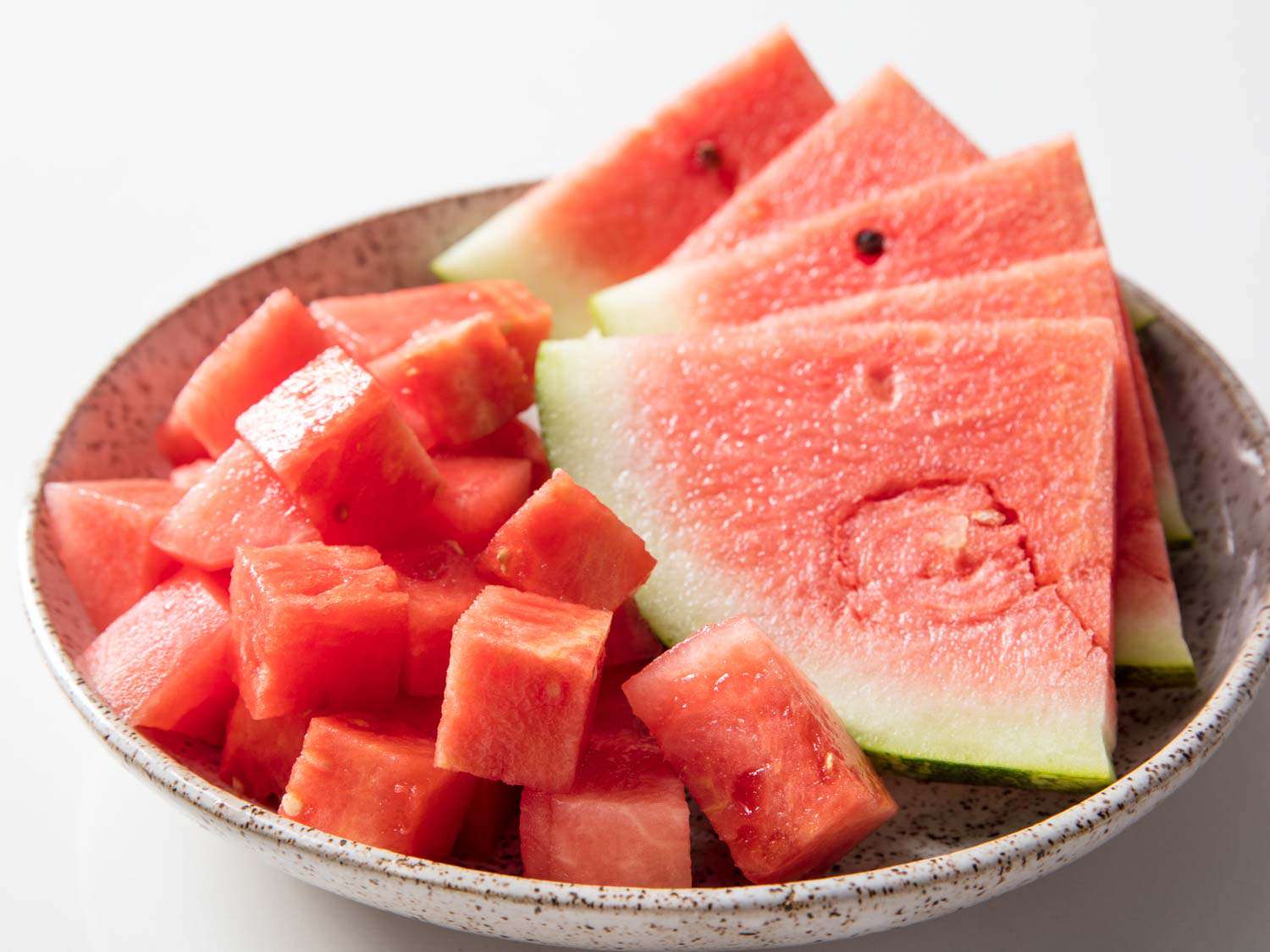 A bowl holding cubed watermelon and five watermelon wedges.