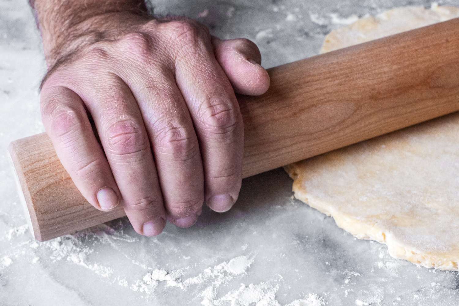 A person using a J.K. Adams Dowel Rolling Pin to flatten dough on a floured surface