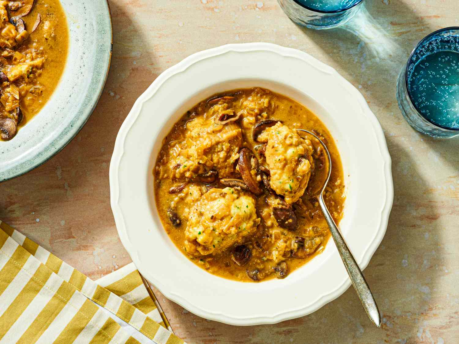 Bowl of mushroom soup with dumplings presented on a table setting including a striped napkin and drinking glasses