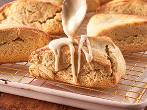 Maple scone being drizzled with glaze displayed on a cooling rack with other scones in the background