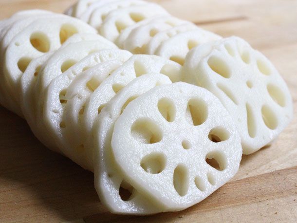 Slices of lotus root shingled on a wooden cutting board.