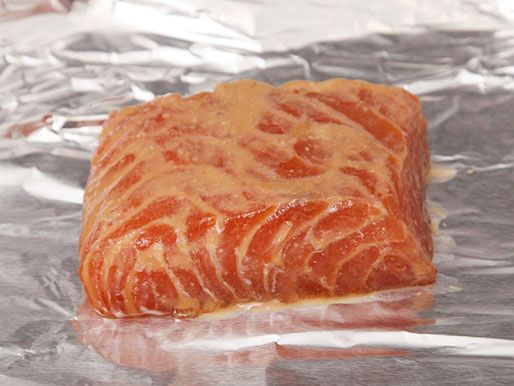 A piece of salmon fillet being marinated in a mixture of miso, soy sauce, sake, and sugar resting on an aluminium foil-lined tray. 
