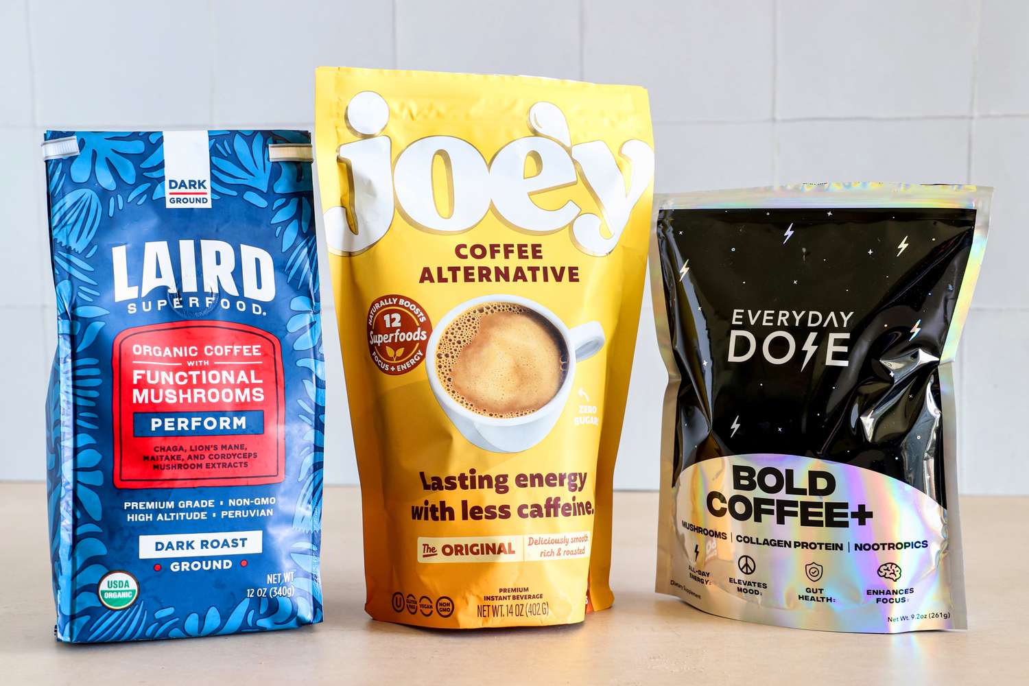 Packages of Laird Superfood, Joe'y, and Everyday Dose mushroom coffees standing side by side on a table.