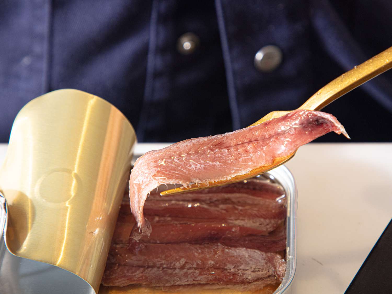 A can of anchovy fillets being served with a golden utensil