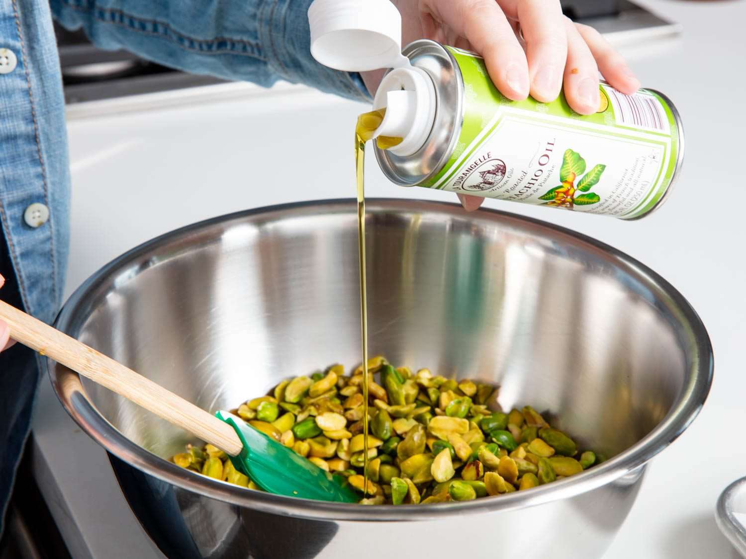 Drizzling pistachio oil over a bowl of blanched and peeled Sicilian pistachios.