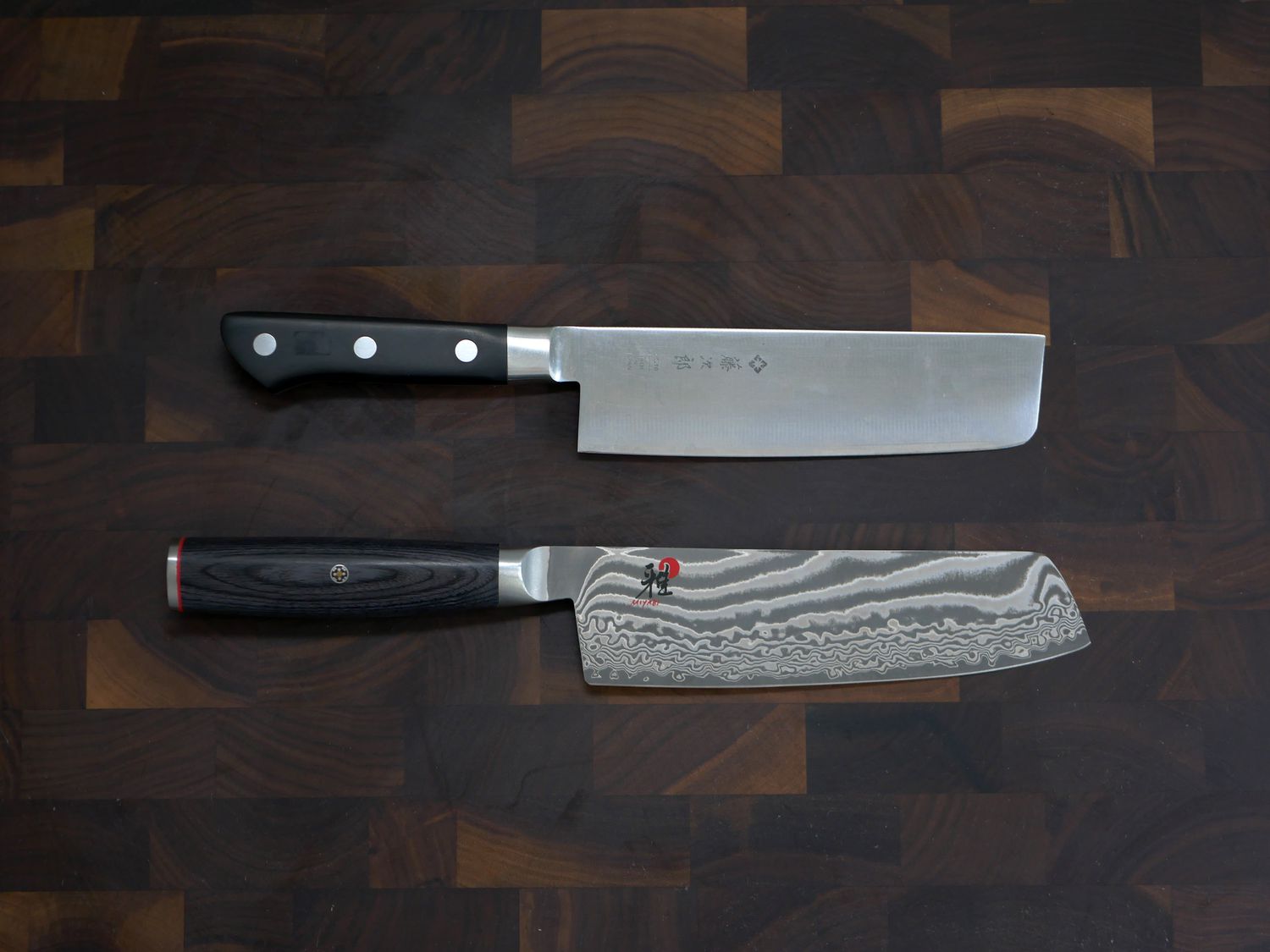 a photo that showcases two nakiri knives, one with a slim handle and the other with a larger, rounded handle