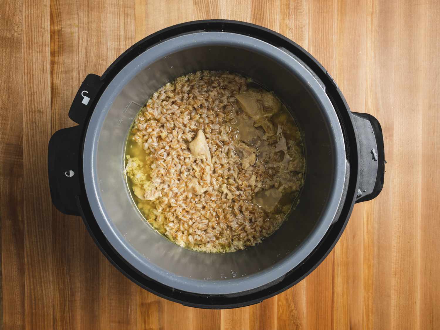 Overhead view of water, farro, and chicken in a pressure cooker