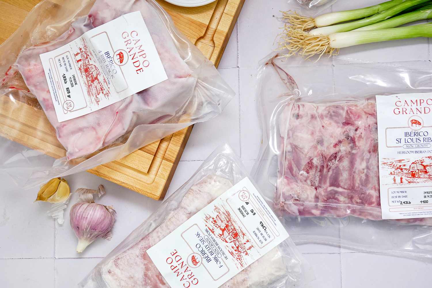 Packaged cuts of Campo Grande Iberico pork displayed near garlic and green onions on a kitchen surface