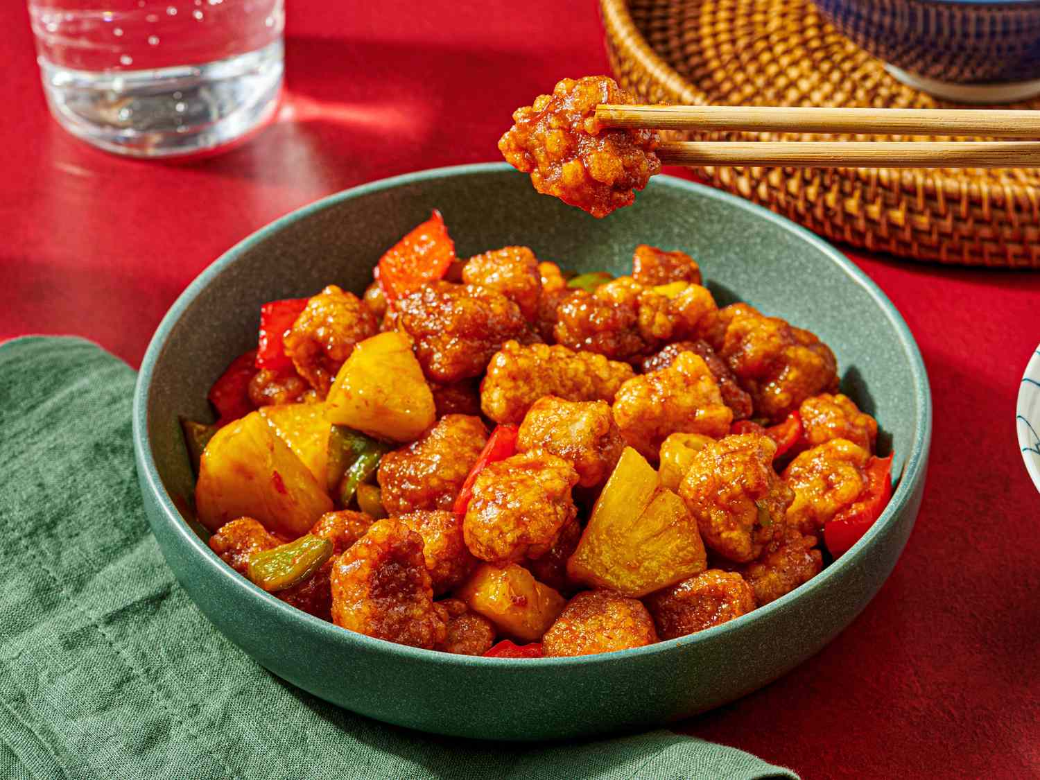 A bowl of Chinese sweet and sour pork with pineapple and vegetables chopsticks holding a piece above the dish