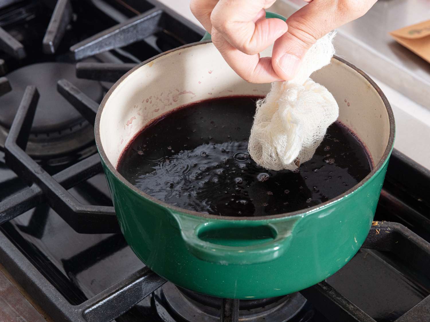 dropping spiced wrapped in cheesecloth into wine in a dutch oven
