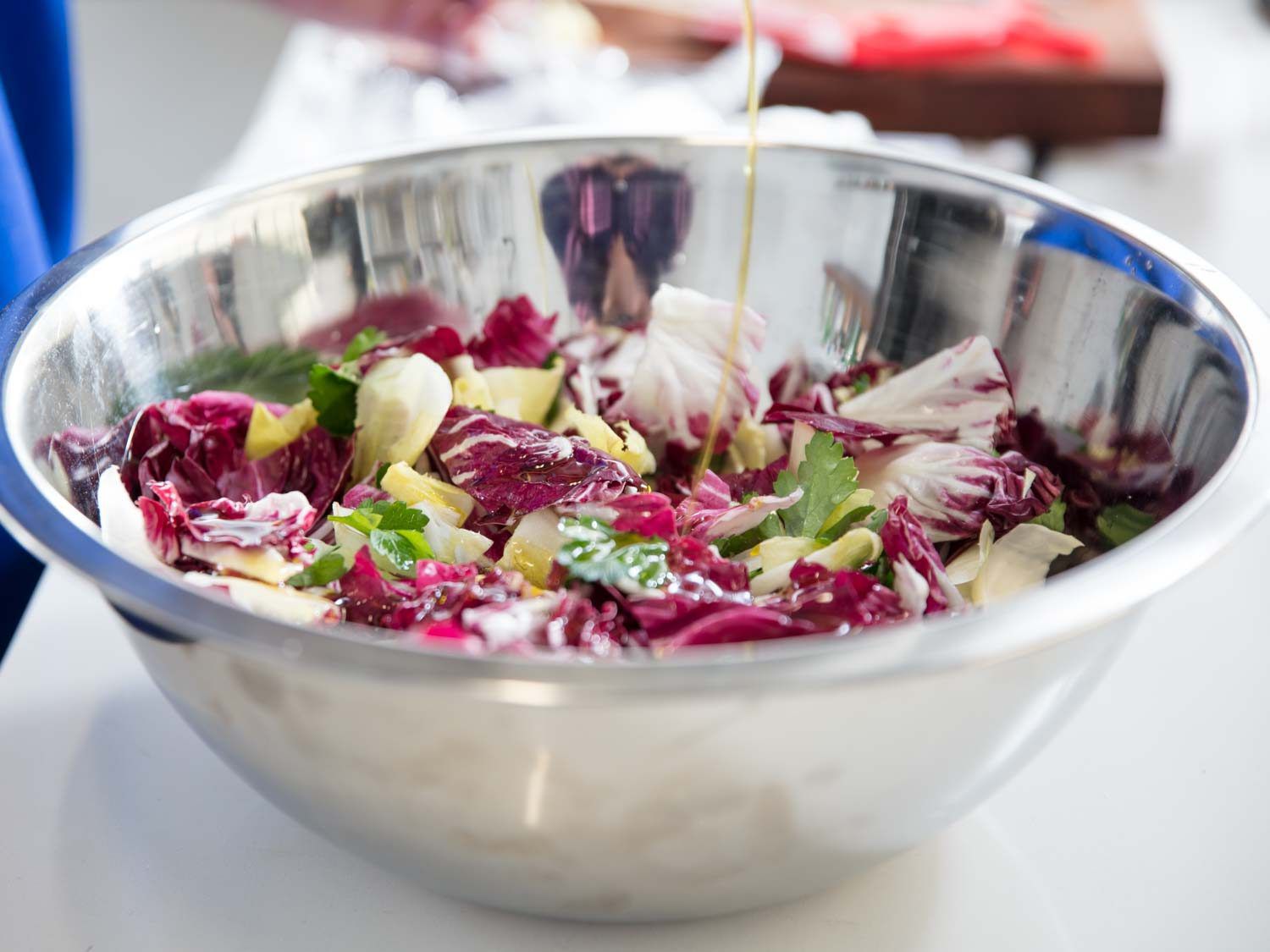 Drizzling olive oil in radicchio, Belgian endive, and parsley in a bowl.