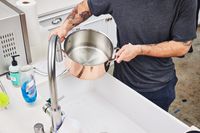 Hands holding Williams Sonoma Thermo-Clad Copper 10-Piece Cookware Set pot near sink