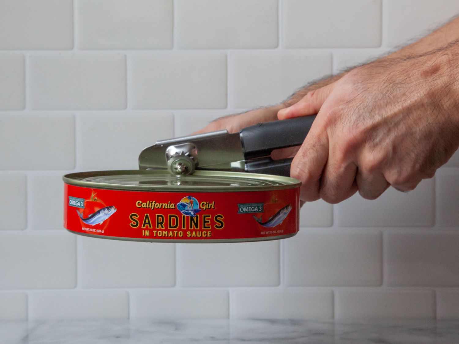 A person using a can opener to open a can of sardines