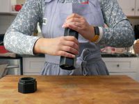 a person using the hexclad pepper mill over a cutting board