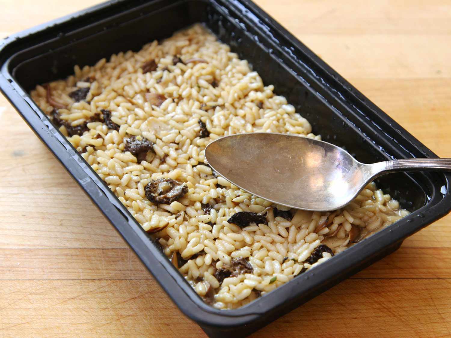 Par-cooked risotto is transferred to a plastic storage container.