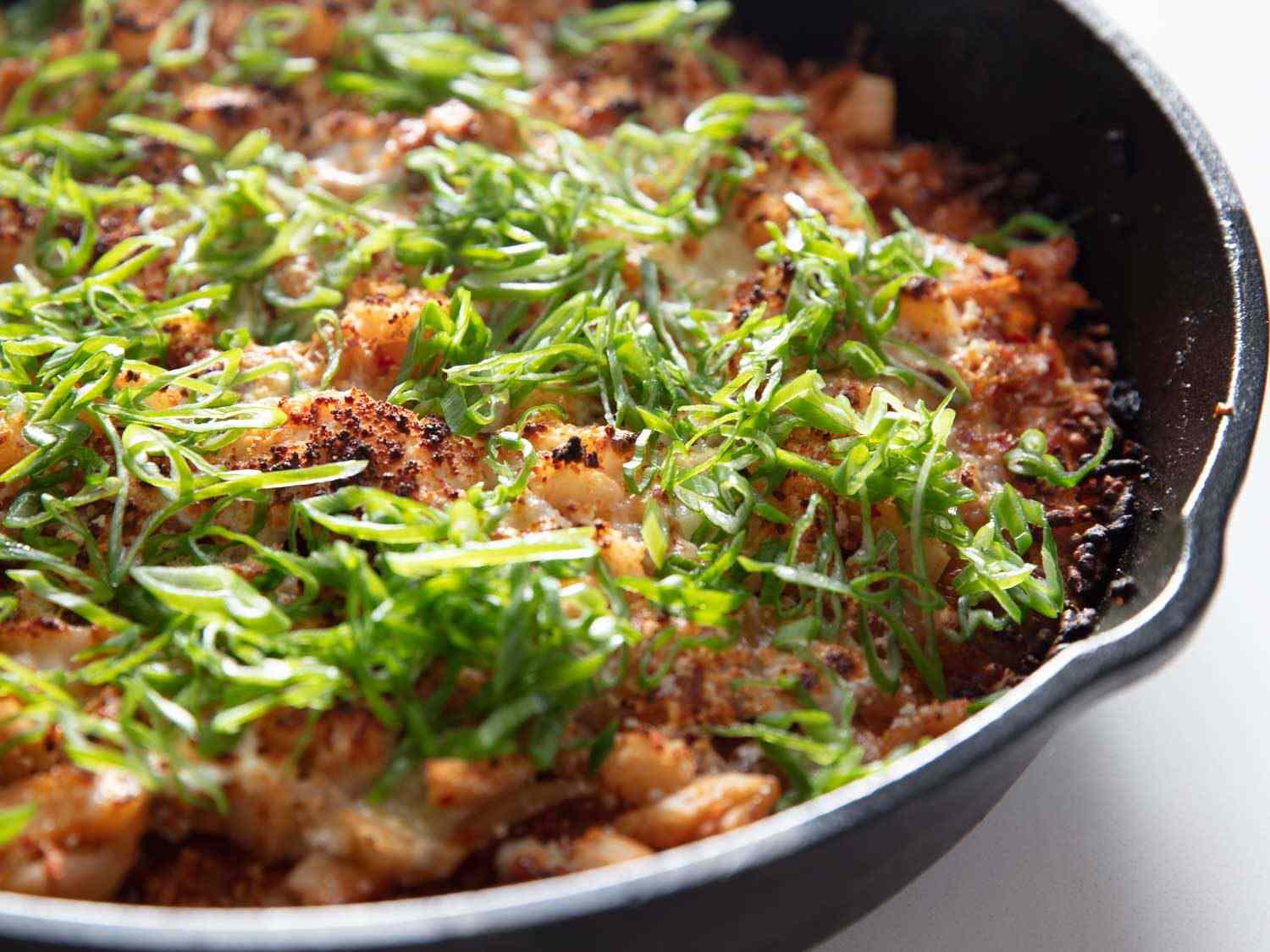 Crispy, cheesy, kimchi-topped rice topped with scallions in a cast iron skillet