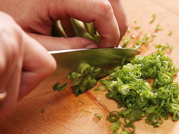 A knife slicing scallions, demonstrating the technique where you pull the knife backward in order to slice.