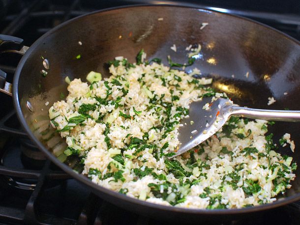 Stir-frying rice, garlic, and chopped greens in a wok together for fried rice.