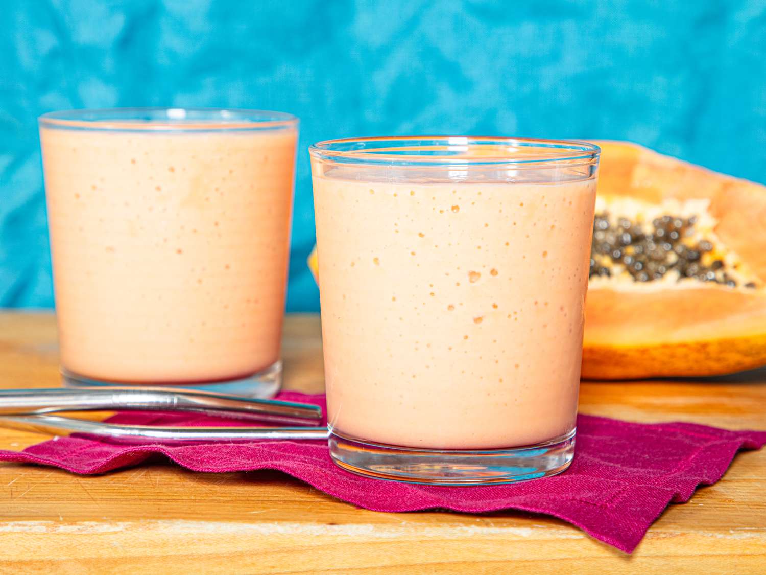 Two glasses of a creamy fruit smoothie a halved papaya rests in the background