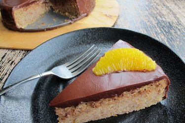 Closeup of a slice of Hazelnut Chocolate Torte With Espresso Ganache served on a black plate, topped with an orange suprême.