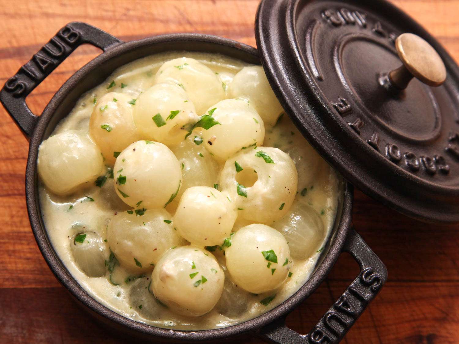 Overhead view of creamed pearl onions in a cast iron cocotte, fresh from the oven.