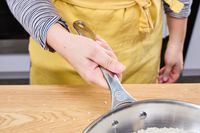 A person holds the handle of the Le Creuset 12 Inch Large Tri-Ply Stainless Steel Fry Pan