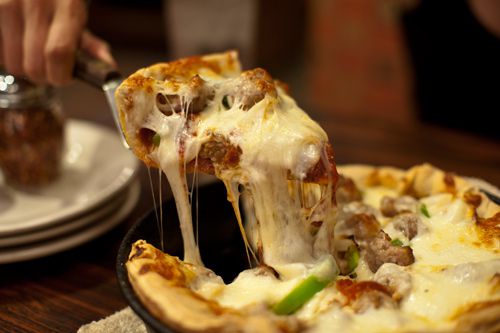Hand pulling out a slice of deep dish sausage pizza from Union Jack Pub in Indianapolis.