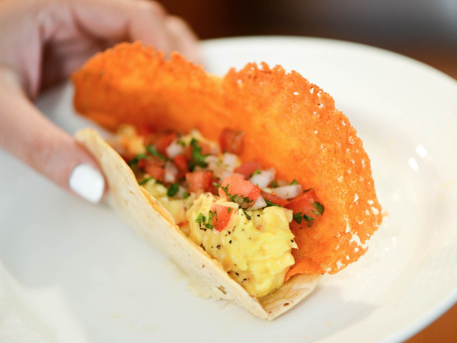 A hand folding over an assembled crispy cheese and egg taco.