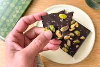 A hand holding a piece of Compartés Salted Pistachio Chocolate Bar