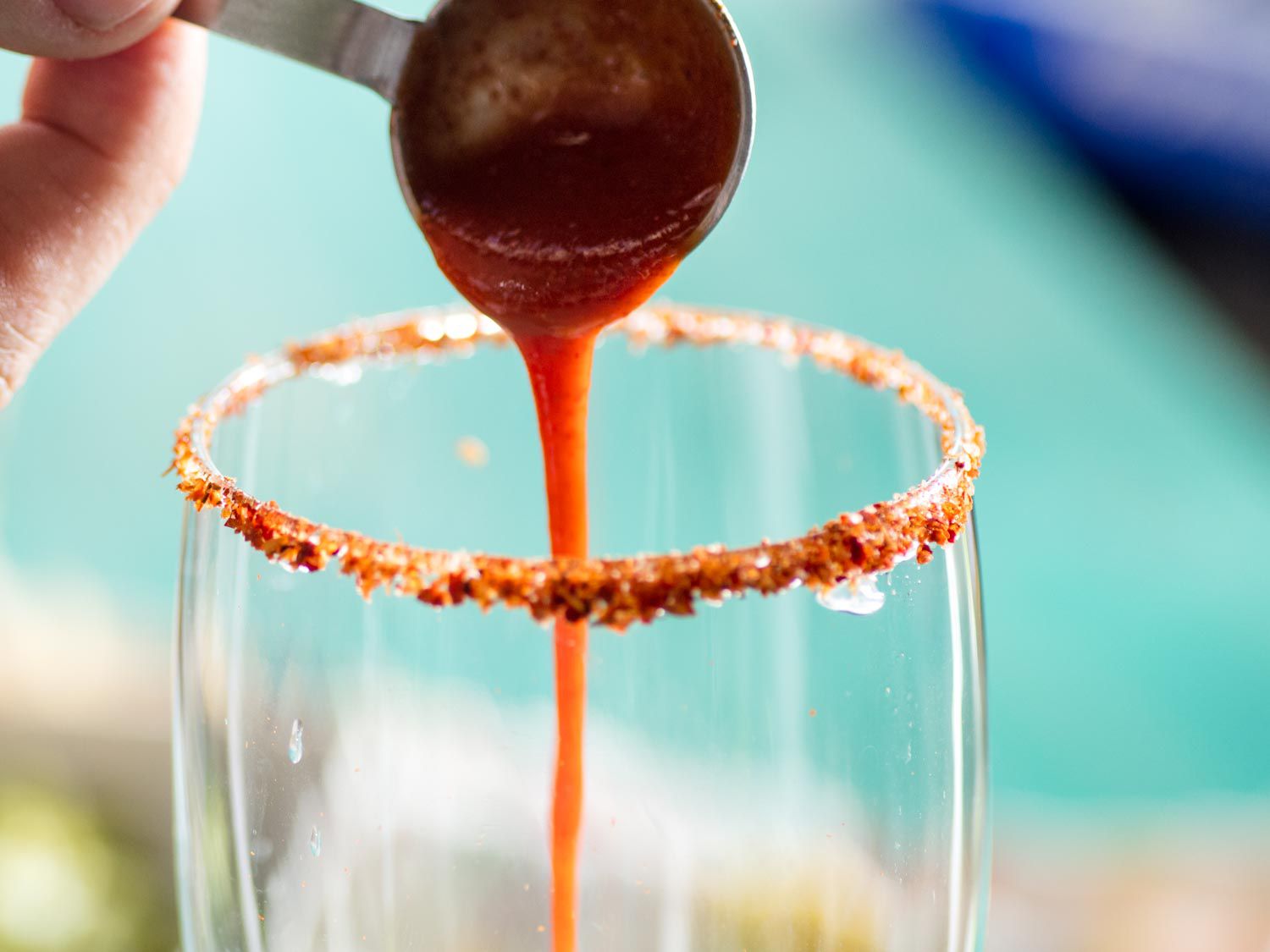 Pouring hot sauce into a Tajín-rimmed glass for a michelada.